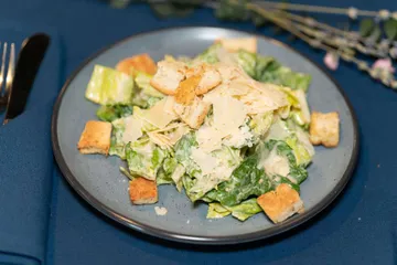 Romaine tossed in Caesar dressing under shaved parmesan, with croutons around the plate