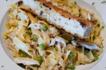 Fettuccine carbonara with chicken, peas and bacon, with a slice of garlic bread