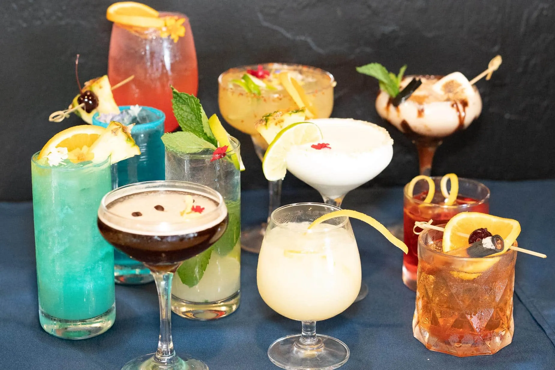 Ten garnished craft cocktails arranged together on the bar