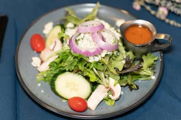 Mixed greens with blue cheese, red onion rings, cucumber, mushrooms and cherry tomatoes, dressing in a silver jug