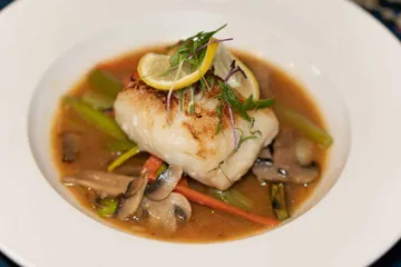 A seared sea bass fillet in miso broth with mushrooms, carrot and scallion, topped with lemon
