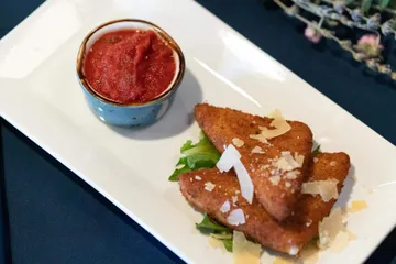 Three fried mozzarella wedges stacked on lettuce under shaved parmesan, with marinara in a blue ramekin