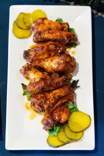 Glazed hot wings lined up on a white plate with dill pickle slices at each end