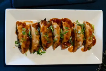Seven potstickers in a row under a glossy chilli sauce, scattered with sliced spring onion
