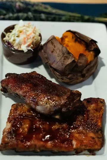 Glazed ribs on a white plate with coleslaw and a baked sweet potato