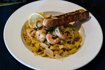 Shrimp over fettuccine with shaved parmesan and basil, a lemon wheel and a slice of garlic bread