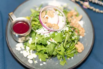 Arugula with crumbled goat cheese, red onion rings and candied walnuts, raspberry vinaigrette in a silver jug